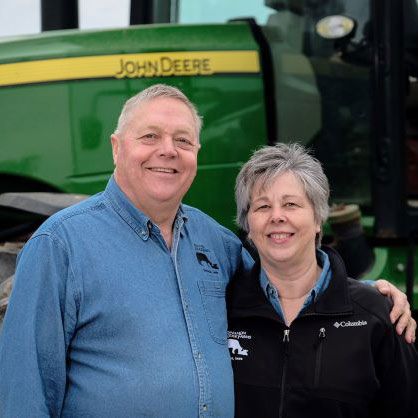 This is a picture of a couple standing infront of a John Deere tractor smiling at the camera